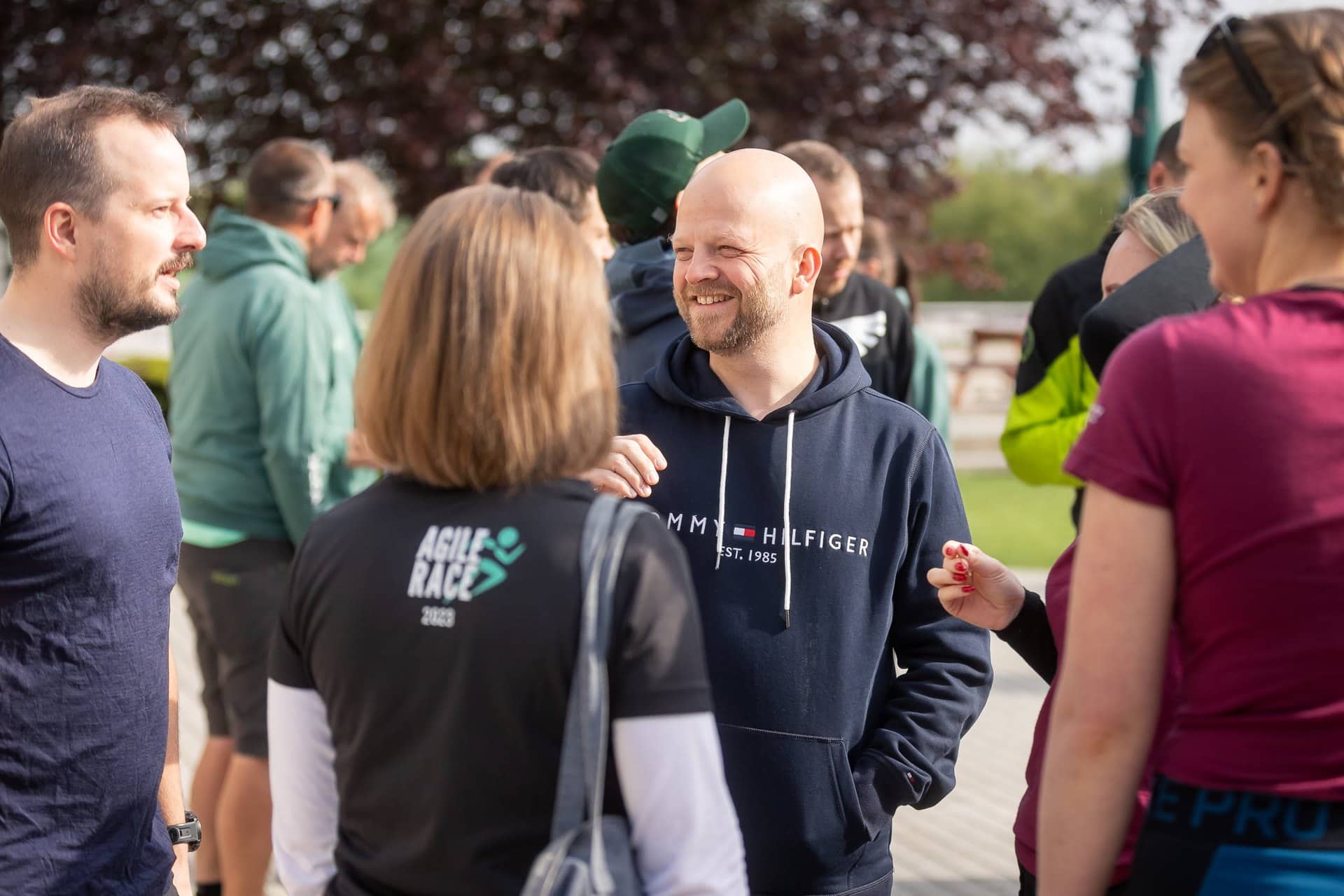 Účastníci v rozhovoru venku na akci Agile Race, jeden v mikině Agile Race